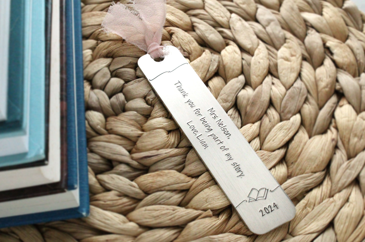 Hand stamped aluminum bookmark, 5" x 1", with text that reads, "Mrs. Nelson, Thank you for being part of my story. Love, Liam. 2024". The bookmark has a pale pink ribbon at the top.